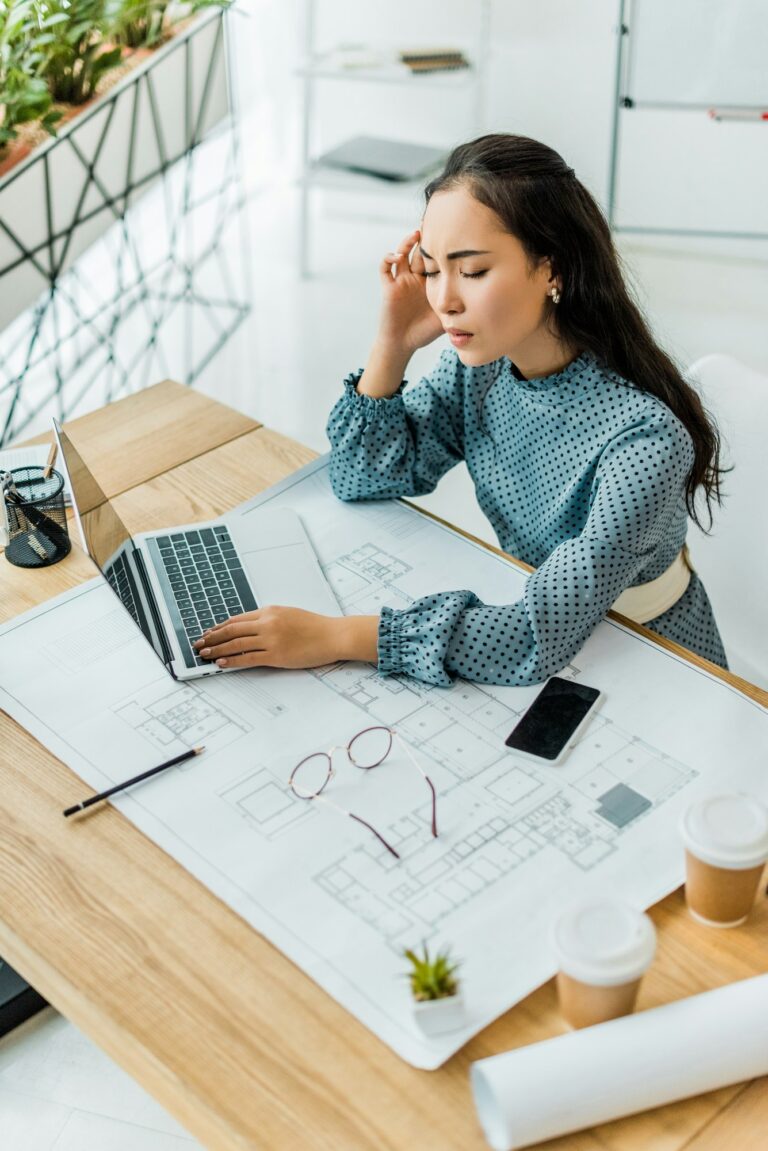 stressed asian female architect having headache while using laptop in office