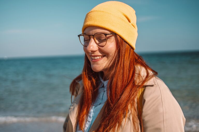 Happy woman 30s smiling while walking by seaside. Enjoying travel and nature concept